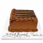A rectangular birthday cake with smooth milk-chocolate brown frosting, piped rosette borders, and chocolate drizzle with gold sprinkles on top, presented on a white board with decorative script text. 1.5kg decorated Forest Fudge birthday cake from Cake Gurus Ruaka