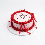 A round birthday cake with white frosting, decorated with red piped borders, red ribbon bows, and small red hearts. The top is written 'TWENTY ATE' in black icing. 1 KG red velvet cake with elegant ribbon decoration, birthday cake from Cake Gurus in Ruaka Nairobi with same day cake delivery