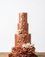 Bronze-colored wedding cake with intricate designs and floral decorations on a white background