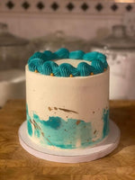 A Blueberry passion round cake with white and blue frosting, decorated with gold sprinkles and a blueberry pattern near the base as a sweet treat by Cake Gurus Ruaka Nairobi with deliveries in Nairobi and its environs.