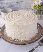 A coconut orange cake with white icing and shredded coconut on the sides, as a sweet treat by Cake Gurus Ruaka Nairobi with deliveries in Nairobi and its environs.