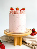 A classic vanilla strawberry cake with pink frosting, adorned with whole strawberries on top, presented on a wooden cake stand. Cake Gurus Ruaka Nairobi