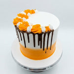 A round frosted cake on a white cake stand, decorated with orange and white piped frosting roses, dark chocolate drip icing, and a bright orange band near the bottom. Fresh Marble Orange birthday cake in Ruaka Nairobi by Cake Gurus, available for same day cake delivery