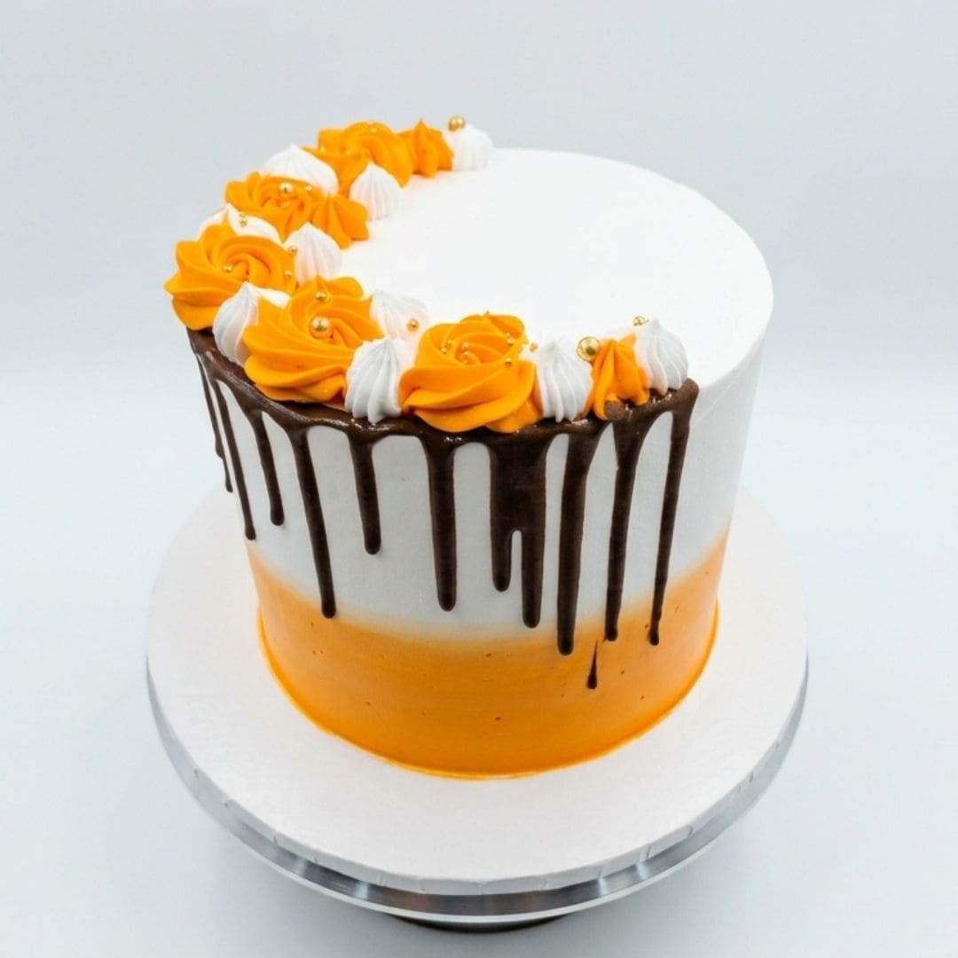 A round frosted cake on a white cake stand, decorated with orange and white piped frosting roses, dark chocolate drip icing, and a bright orange band near the bottom. Fresh Marble Orange birthday cake in Ruaka Nairobi by Cake Gurus, available for same day cake delivery