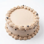 A round cake with light beige frosting, decorated with piped shell-like borders and small dark pearls, shown on a plain white background. Marble Orange Cake by Cake Gurus, fresh birthday cake in Ruaka Nairobi with same day delivery