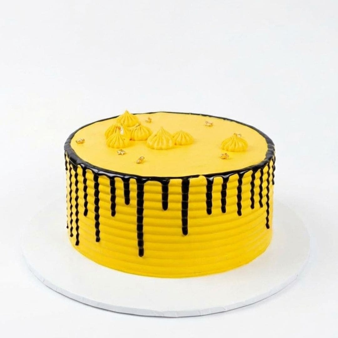 A round yellow frosted cake with black drip decoration on the sides and top, decorated with small piped yellow mounds and gold sprinkles, shown on a white cake board against a white background. Pina Colada Birthday Cake with tropical pineapple and coconut flavours in Nairobi, freshly baked by Cake Gurus