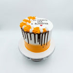 A round birthday cake with a white and orange gradient, decorated with orange and white rosettes, chocolate drip icing, and the text 'MY PARENTS ARE A BLESSING' on top, displayed on a white cake stand against a light gray background. 2 KG Vanilla Lemon Cake with elegant decoration from Cake Gurus in Ruaka Nairobi, fresh birthday cake with same day delivery