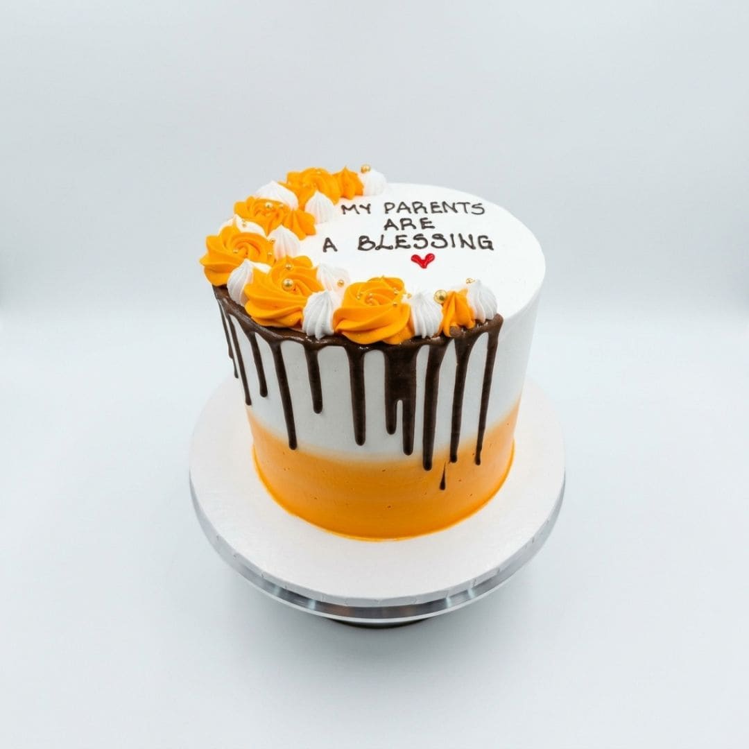 A round birthday cake with a white and orange gradient, decorated with orange and white rosettes, chocolate drip icing, and the text 'MY PARENTS ARE A BLESSING' on top, displayed on a white cake stand against a light gray background. 2 KG Vanilla Lemon Cake with elegant decoration from Cake Gurus in Ruaka Nairobi, fresh birthday cake with same day delivery