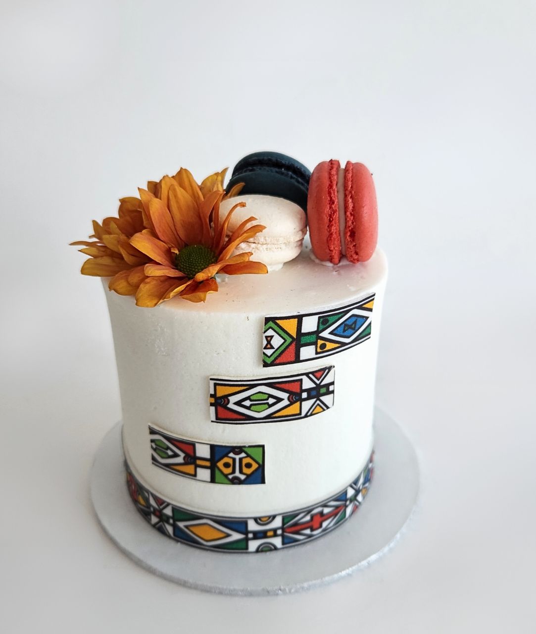 Small cake with decorative patterns, flowers, and macarons on a white background