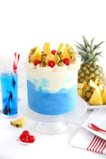 A Piña Colada Blueberry Cake with blue and white layers, topped with pineapple, coconut, and blueberries, served on a white plate,  as a sweet treat by Cake Gurus Ruaka Nairobi with deliveries in Nairobi and its environs.